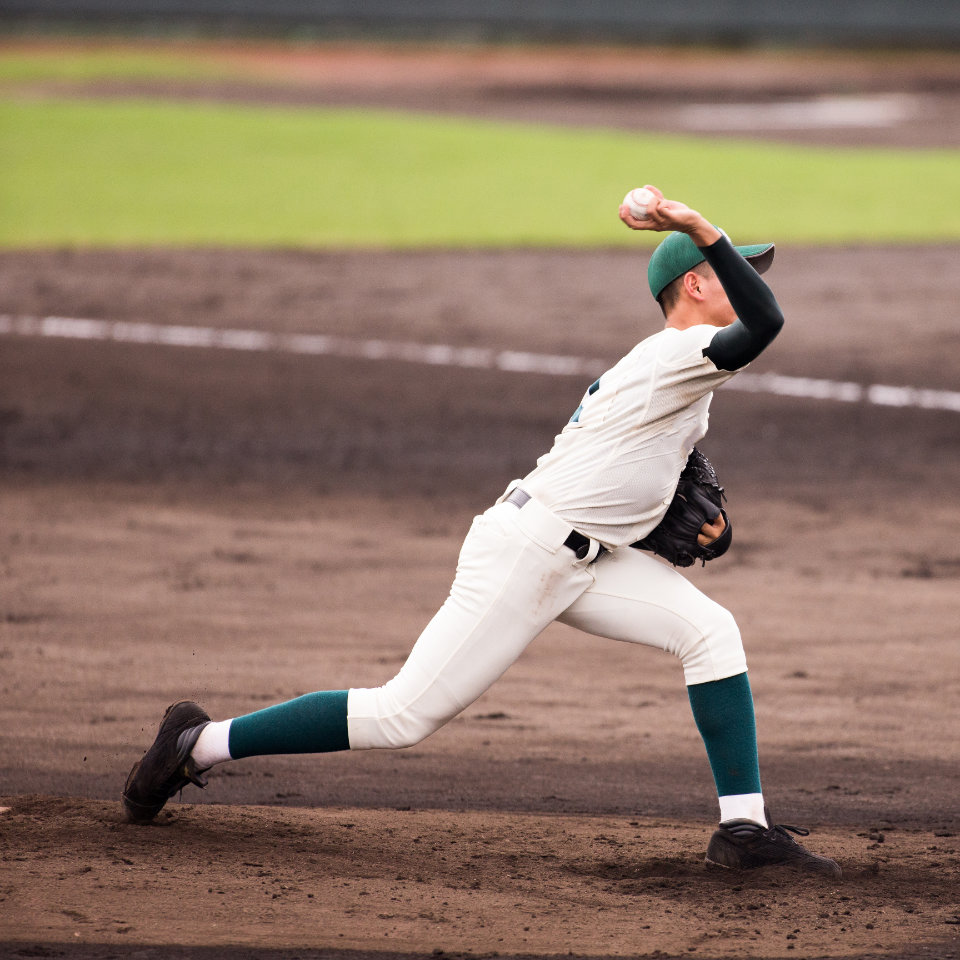 A baseball pitcher in a white and green uniform throws a pitch on a dirt and grass field.