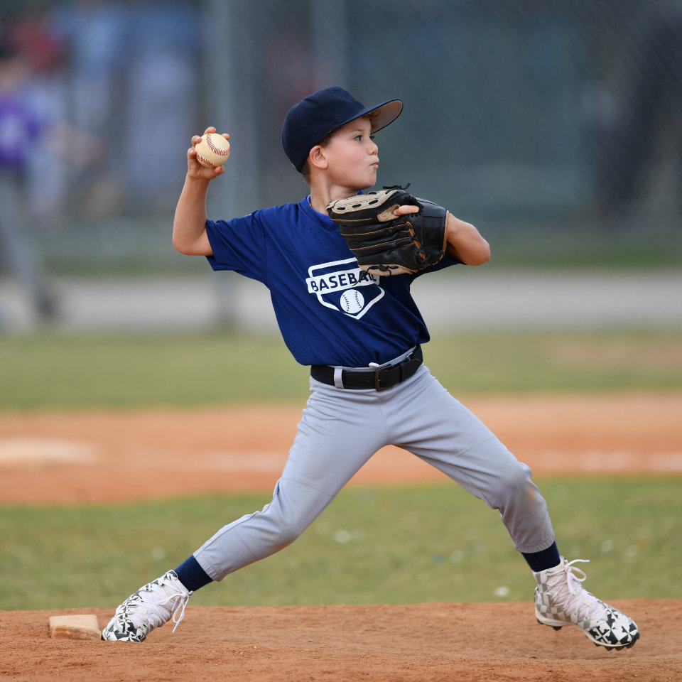 A young boy in a blue shirt and gray pants prepares to throw a baseball on a baseball field.