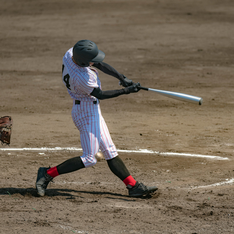 A baseball player in a striped uniform and black helmet swings a bat during a game, making contact with the ball on a dirt field.