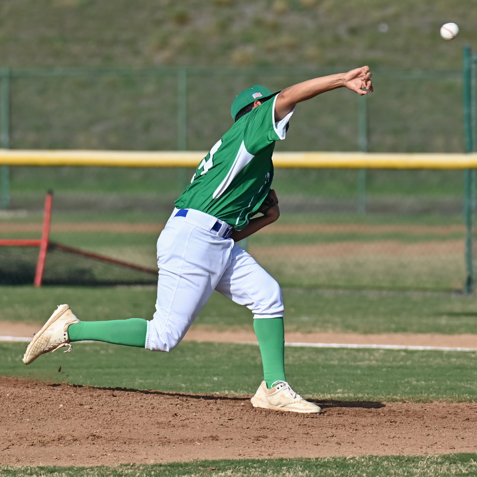 A baseball player in a green and white uniform throws a pitch on a baseball field.