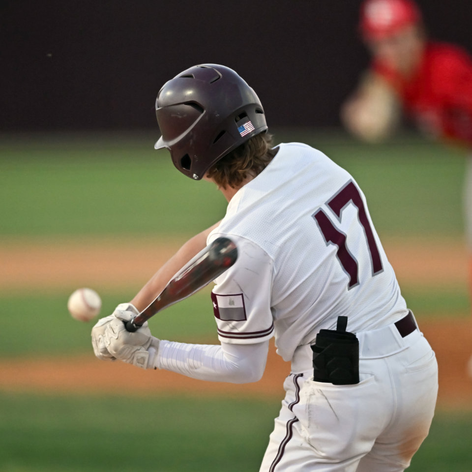 Baseball player in a white uniform with number 17 swings at an incoming pitch during a game; another player in red is visible in the background.
