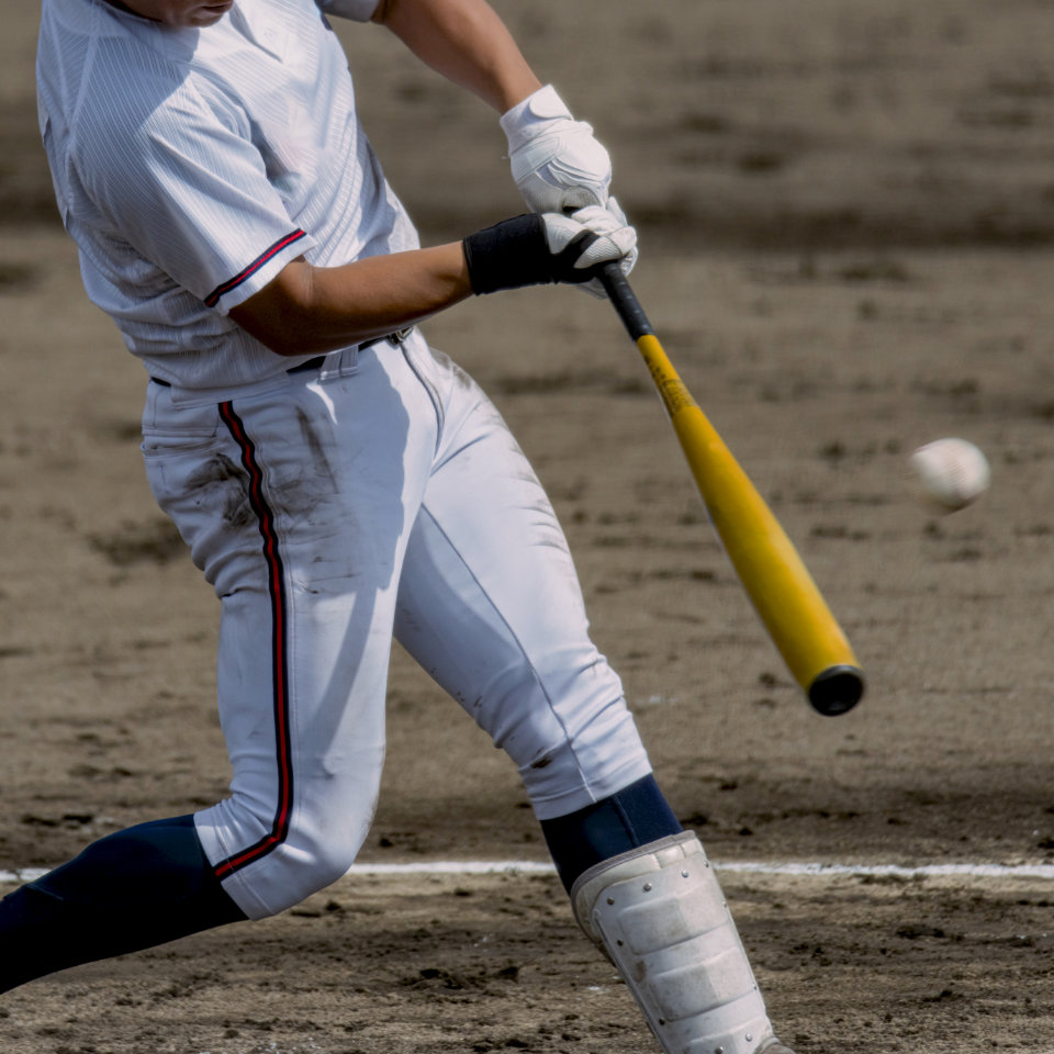 Baseball player in white uniform swinging a yellow bat at a pitched ball on a dirt field.