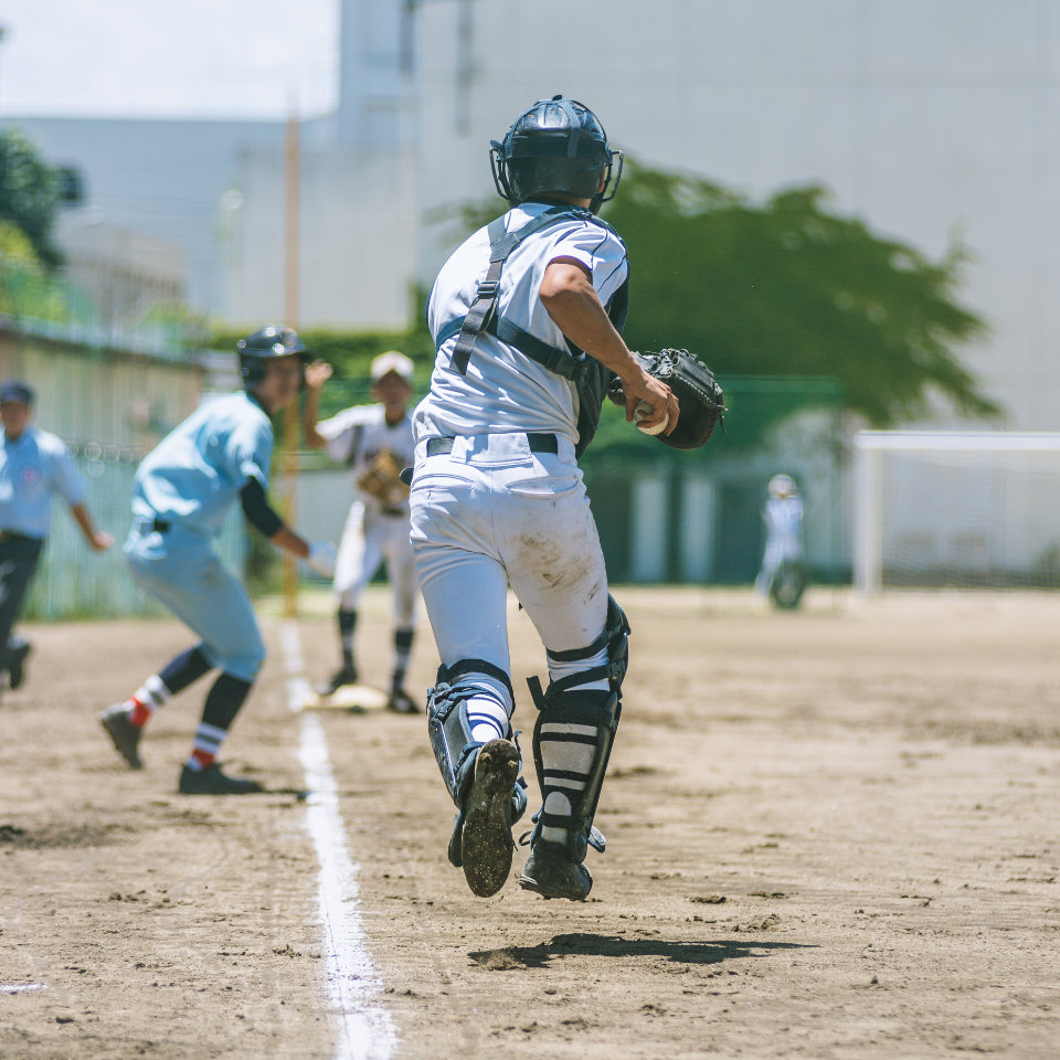 A baseball catcher runs toward home plate as a player in blue sprints along the baseline during a game on a dirt field.