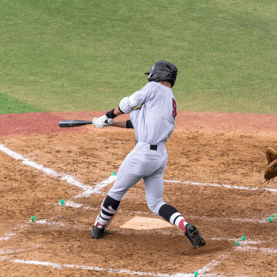 A baseball player in a gray uniform swings a bat at home plate during a game on a dirt and grass field.