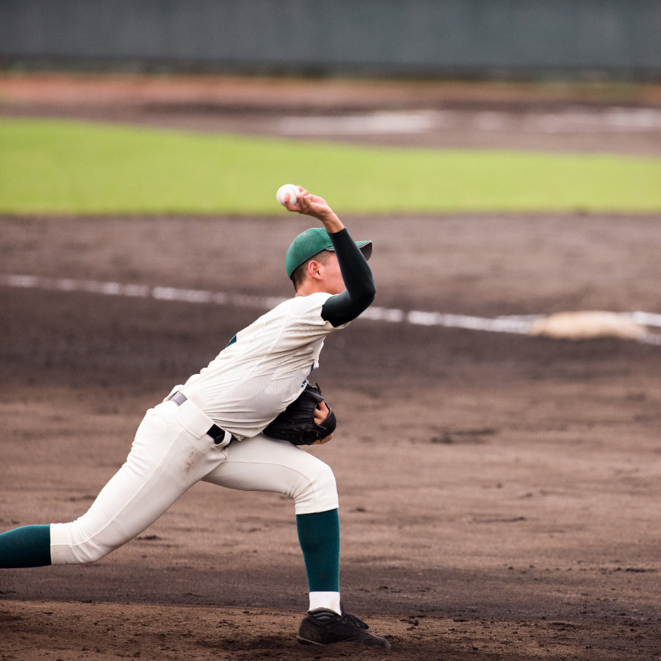 A baseball pitcher in a white and green uniform winds up to throw a pitch on a dirt baseball field.