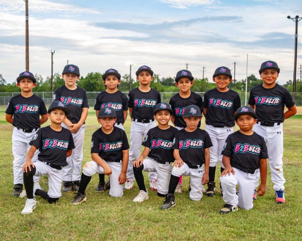 B2B Elite Team posed outdoors on a grassy field, dressed in matching black shirts and white pants, arranged in two rows — some kneeling in front and others standing behind.