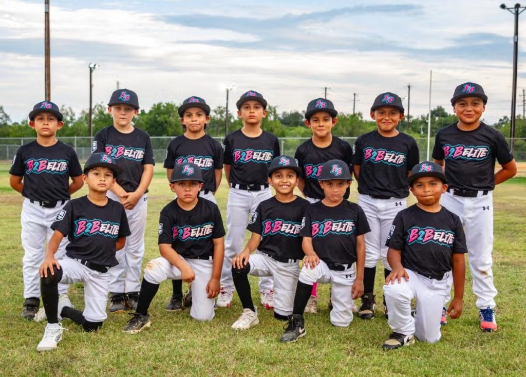 B2B Elite Team posed outdoors on a grassy field, dressed in matching black shirts and white pants, arranged in two rows — some kneeling in front and others standing behind.