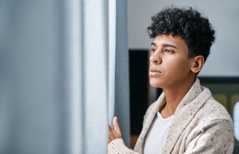 Home, thinking and man by window with social anxiety, reflection or winter burnout. Depression, mental health and tired person in bedroom for emotional stress, decision or planning in apartment